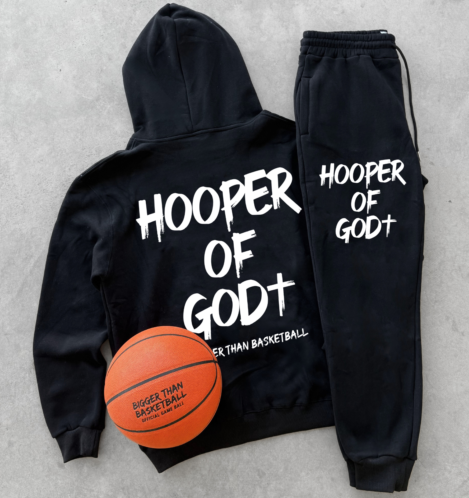 Black hoodie and jogger set with 'Hooper of Godt' text, accompanied by a basketball on a concrete surface.